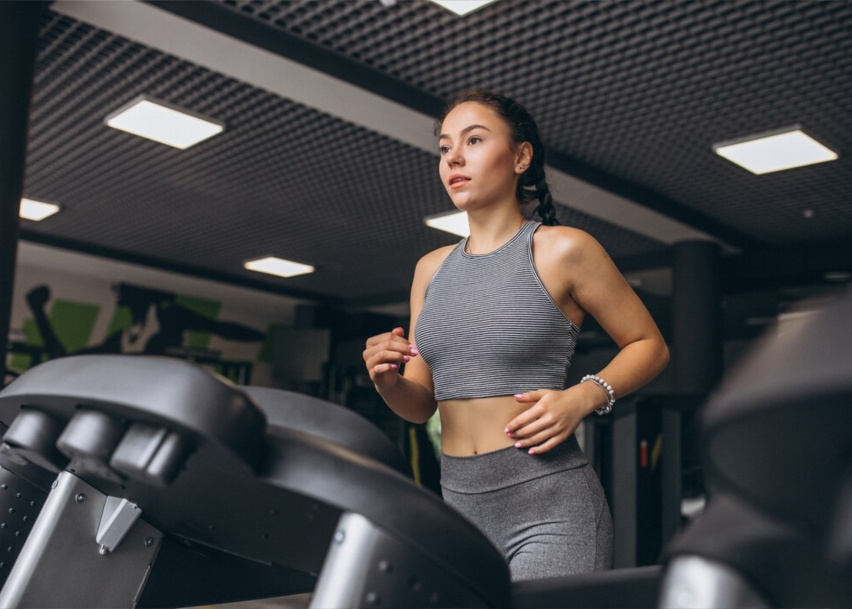 Изображен спортивный зал где на главном фоне находится девушка, что бежит по велодорожке.